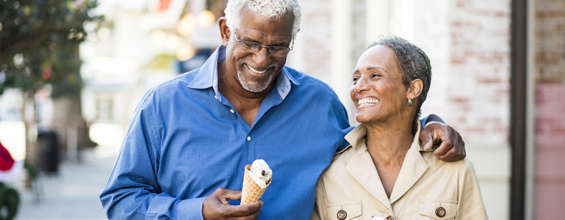 older couple walks down city sidewalk while holding ice cream cones