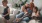 mother sits on a couch with her daughters while her son plays a video game
